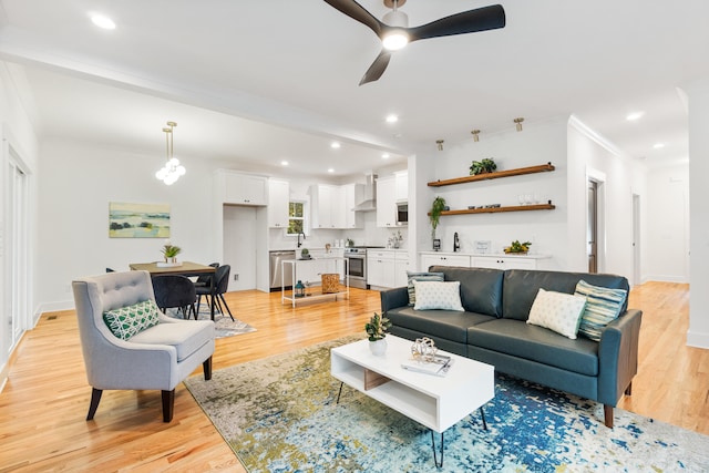 living room featuring light wood-type flooring, ceiling fan, and crown molding