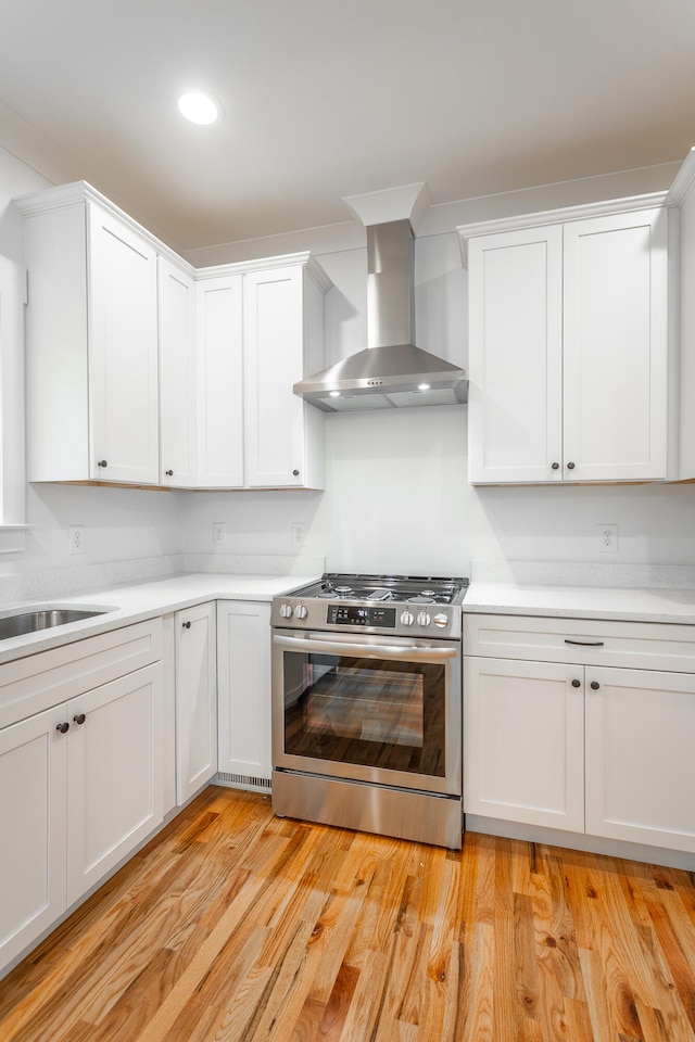 kitchen featuring stainless steel stove, white cabinetry, wall chimney exhaust hood, and light hardwood / wood-style floors