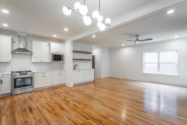 kitchen featuring light hardwood / wood-style flooring, white cabinets, wall chimney range hood, and appliances with stainless steel finishes