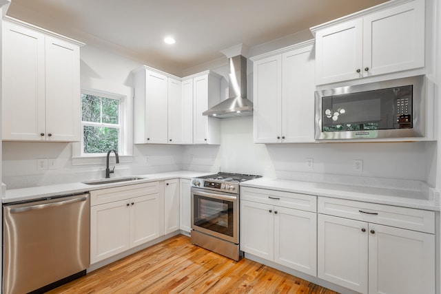 kitchen with sink, wall chimney exhaust hood, appliances with stainless steel finishes, light hardwood / wood-style floors, and white cabinetry