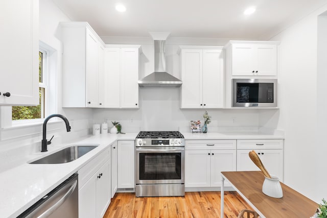 kitchen featuring white cabinets, wall chimney range hood, sink, light hardwood / wood-style floors, and stainless steel appliances