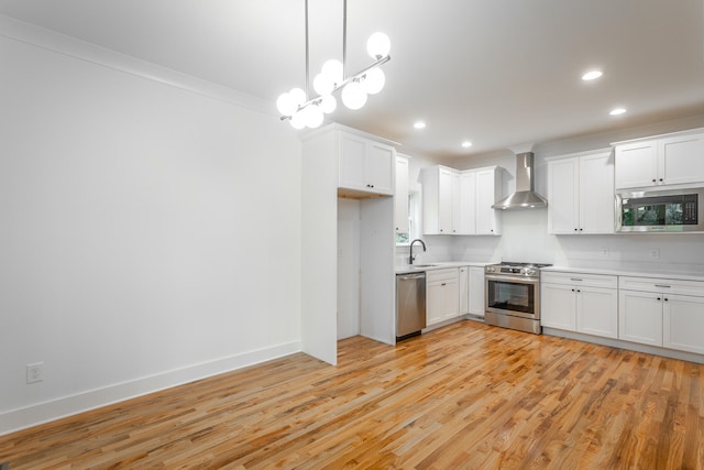 kitchen with white cabinetry, hanging light fixtures, wall chimney range hood, appliances with stainless steel finishes, and light wood-type flooring