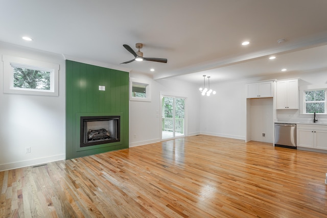 unfurnished living room featuring ceiling fan with notable chandelier, a large fireplace, light wood-type flooring, and sink