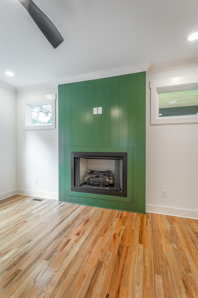 interior details featuring hardwood / wood-style flooring, ceiling fan, a large fireplace, and crown molding