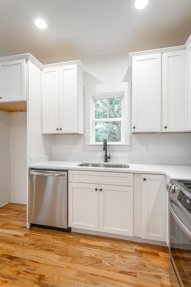 kitchen with white cabinets, appliances with stainless steel finishes, light hardwood / wood-style flooring, and sink