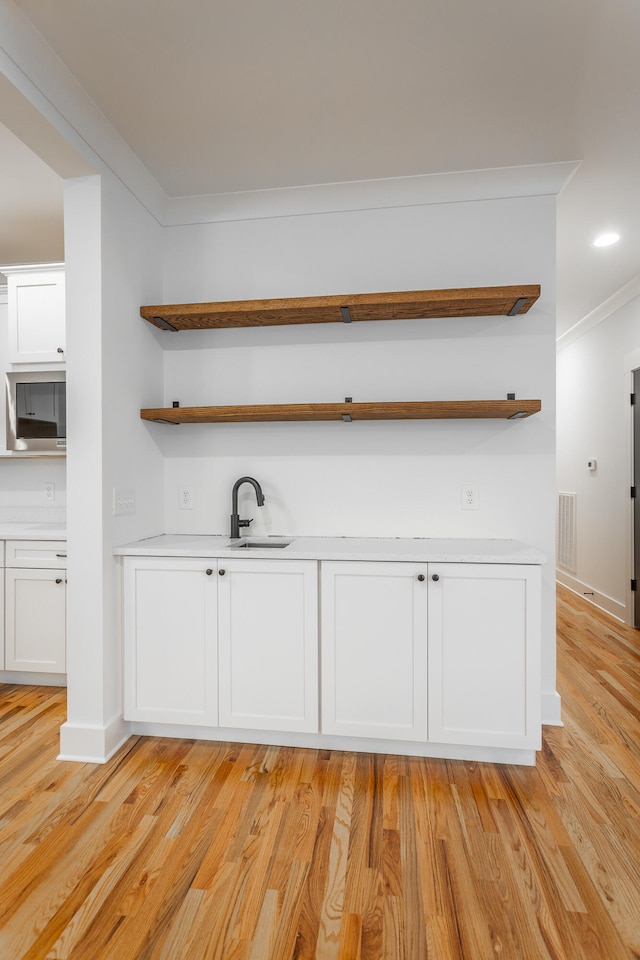 bar featuring light hardwood / wood-style floors, crown molding, white cabinetry, and sink