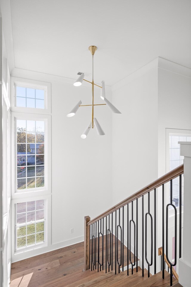 stairway featuring hardwood / wood-style floors, a notable chandelier, and ornamental molding