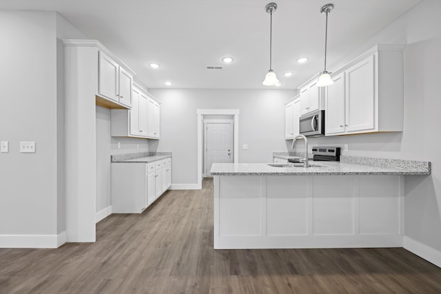 kitchen with stainless steel microwave, hanging light fixtures, white cabinets, a sink, and light stone countertops