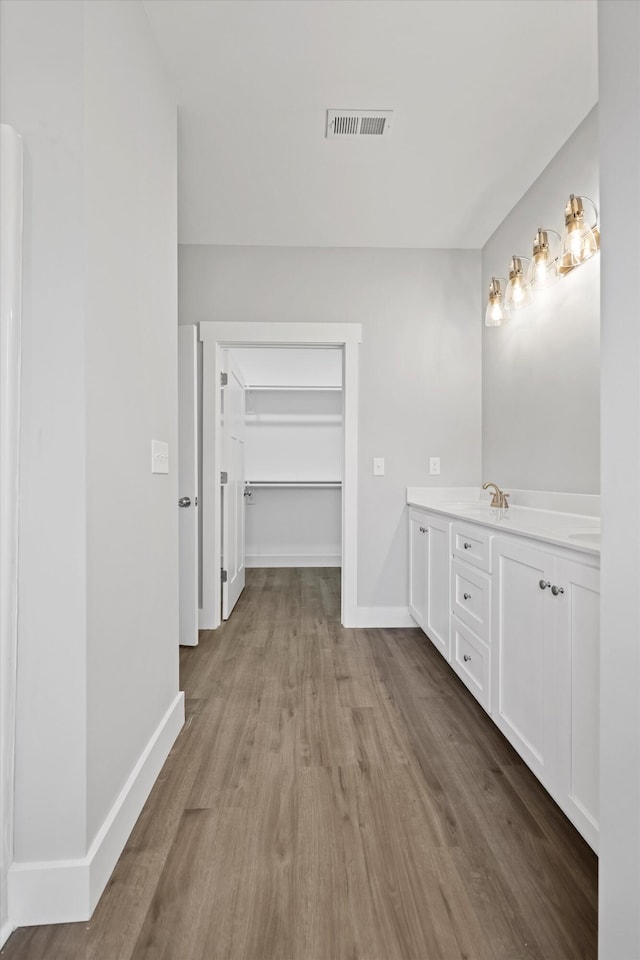 bathroom featuring double vanity, baseboards, visible vents, wood finished floors, and a spacious closet