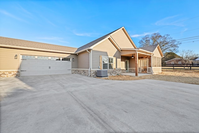 view of front of home featuring central AC unit, an attached garage, fence, concrete driveway, and stone siding