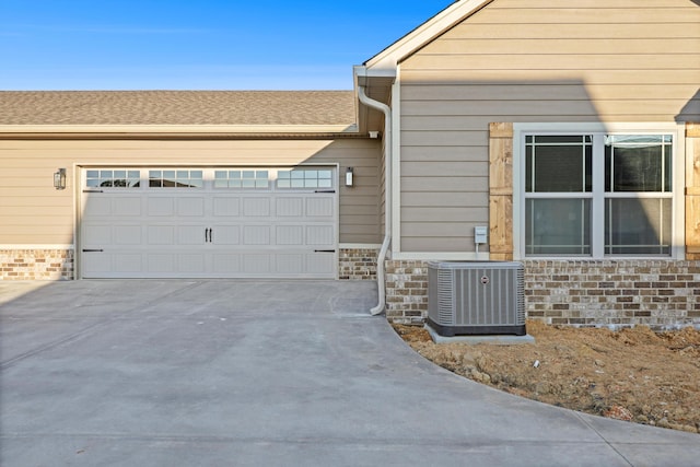 view of home's exterior with driveway, central AC unit, roof with shingles, and an attached garage