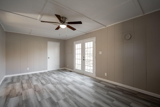 empty room featuring ceiling fan, light wood-type flooring, wooden walls, and french doors