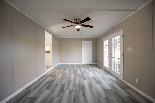 empty room featuring french doors, light wood-type flooring, ceiling fan, and wood walls