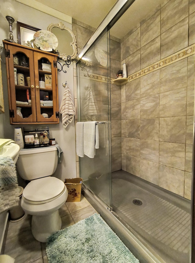 bathroom with toilet, tile patterned floors, and a shower with shower door