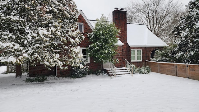 snow covered property featuring fence, brick siding, and a chimney