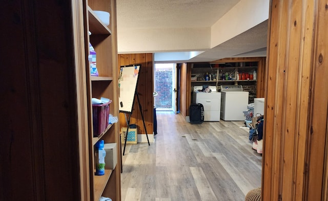 below grade area with wooden walls, light wood-style flooring, a textured ceiling, and independent washer and dryer