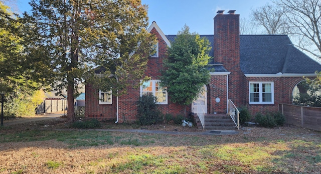 view of front of home with fence, roof with shingles, a front yard, brick siding, and a chimney