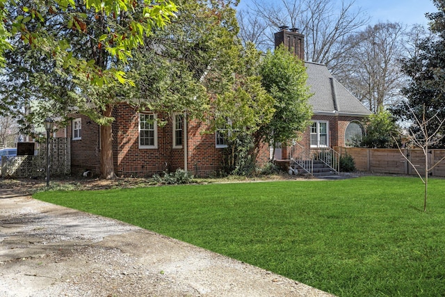 exterior space featuring brick siding, fence, a chimney, a yard, and driveway