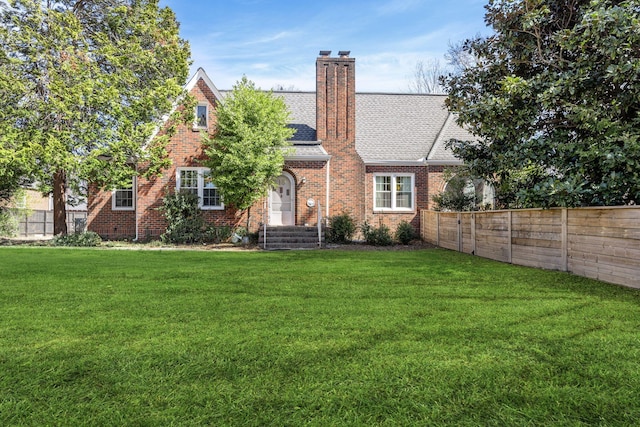 back of house featuring brick siding, a lawn, roof with shingles, and fence