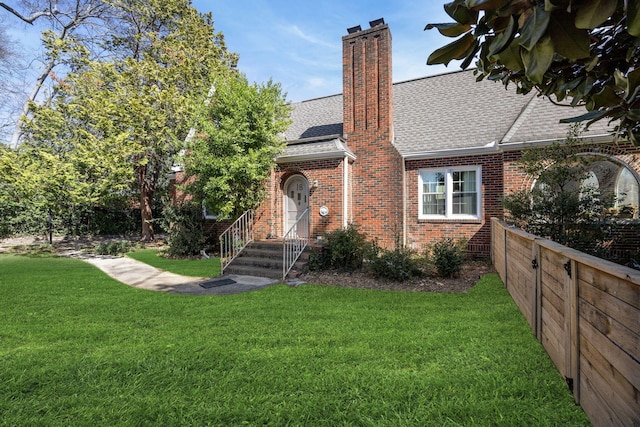 view of front facade featuring a chimney, brick siding, roof with shingles, and a front lawn