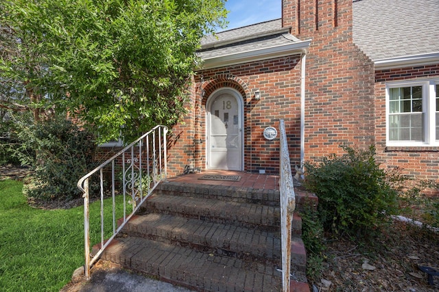 entrance to property with brick siding and a shingled roof