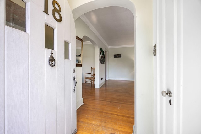 hall with baseboards, arched walkways, light wood-style flooring, and crown molding