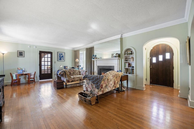 living area with hardwood / wood-style flooring, crown molding, a warm lit fireplace, and a textured ceiling