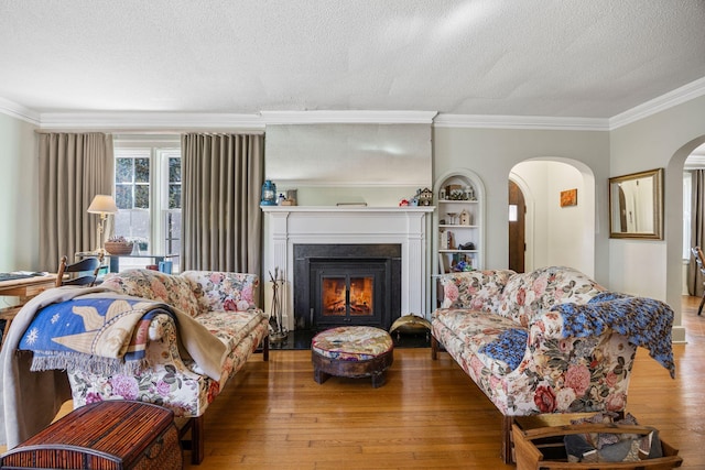 living area with wood finished floors, arched walkways, ornamental molding, and a textured ceiling