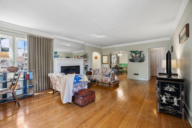 living area with baseboards, ornamental molding, a warm lit fireplace, hardwood / wood-style flooring, and arched walkways