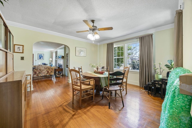 dining space featuring a ceiling fan, arched walkways, wood-type flooring, and ornamental molding