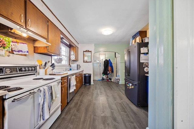 kitchen featuring dark wood-style floors, arched walkways, stainless steel appliances, light countertops, and brown cabinets