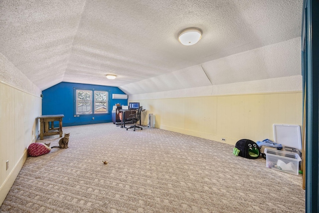 recreation room with a wall unit AC, a textured ceiling, carpet flooring, and vaulted ceiling