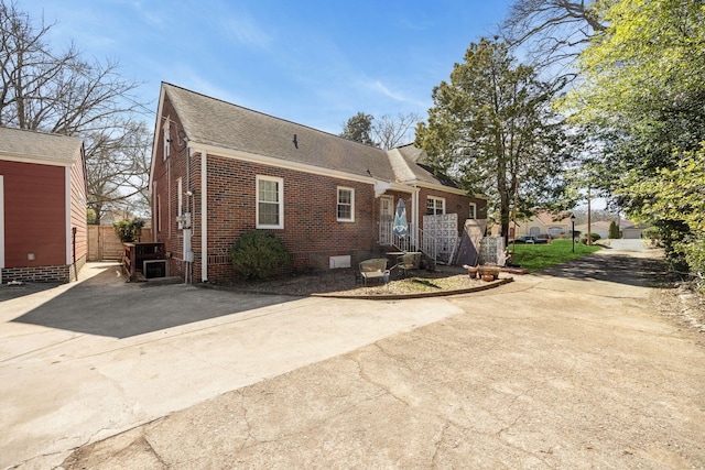 view of front facade with brick siding, concrete driveway, roof with shingles, and fence