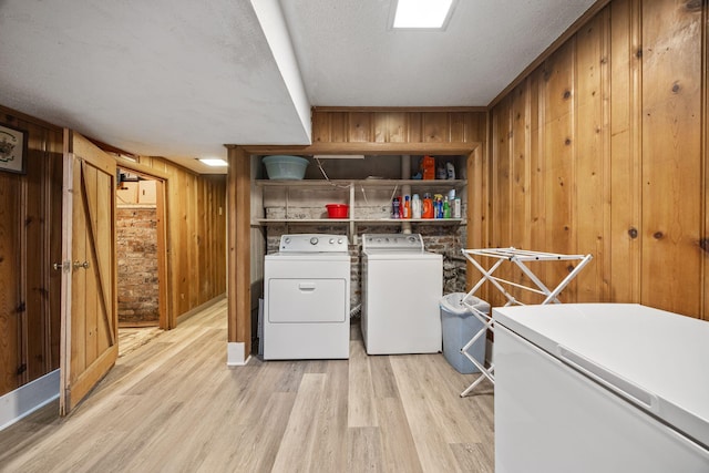 laundry room featuring wooden walls, washing machine and clothes dryer, laundry area, a textured ceiling, and light wood-type flooring