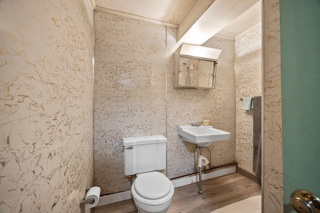 half bathroom with crown molding, toilet, wood finished floors, and a sink