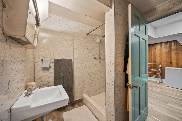 bathroom with wood finished floors, a tile shower, and a sink