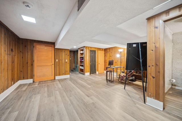 interior space featuring light wood finished floors, wooden walls, baseboards, stairway, and a textured ceiling