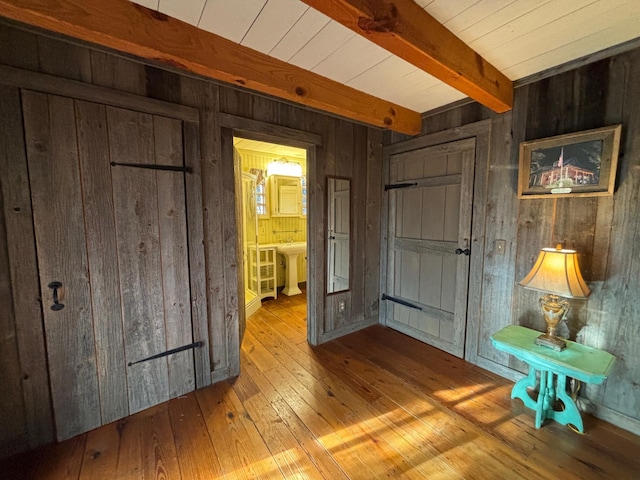 unfurnished bedroom with beam ceiling, wooden walls, light hardwood / wood-style flooring, and ensuite bathroom