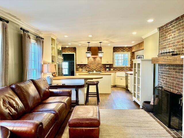 living room featuring light wood-type flooring, crown molding, and a brick fireplace