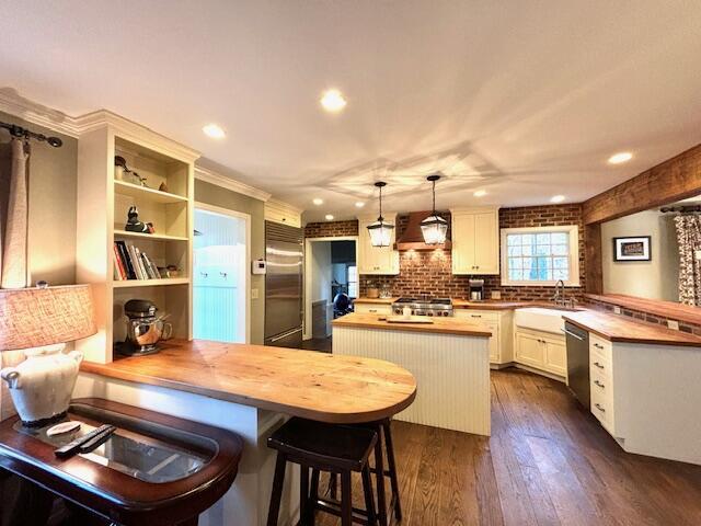 kitchen with dark hardwood / wood-style flooring, stainless steel appliances, decorative light fixtures, a center island, and butcher block counters