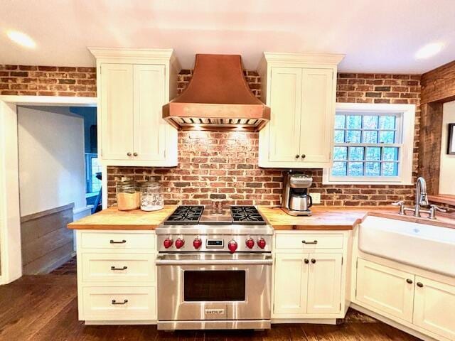 kitchen featuring dark hardwood / wood-style flooring, premium range hood, brick wall, designer range, and sink