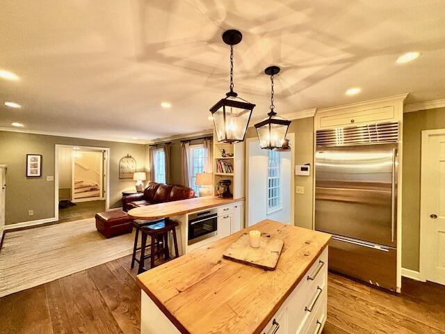 kitchen featuring pendant lighting, butcher block counters, wood-type flooring, appliances with stainless steel finishes, and white cabinetry