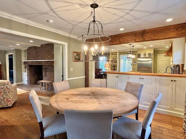 dining room with light wood-type flooring, ornamental molding, sink, beamed ceiling, and a fireplace