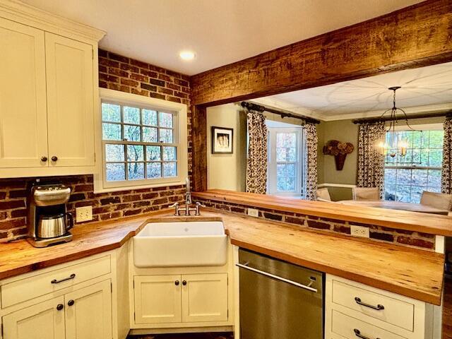 kitchen with pendant lighting, butcher block counters, sink, stainless steel dishwasher, and kitchen peninsula