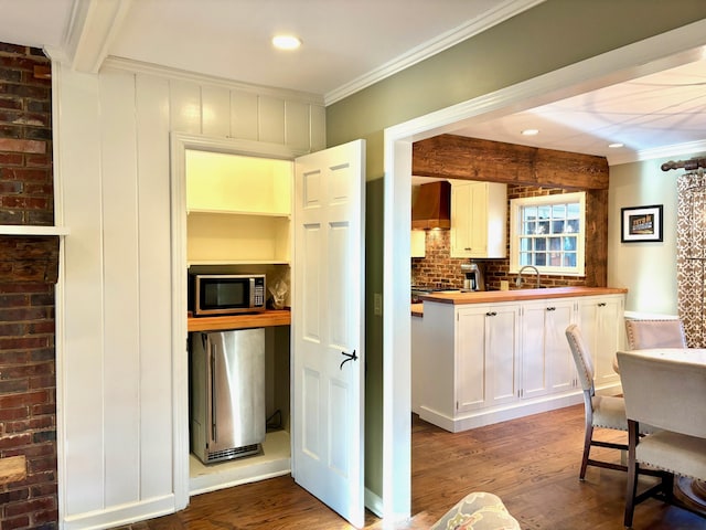 kitchen with white cabinetry, stainless steel appliances, wall chimney range hood, and hardwood / wood-style flooring