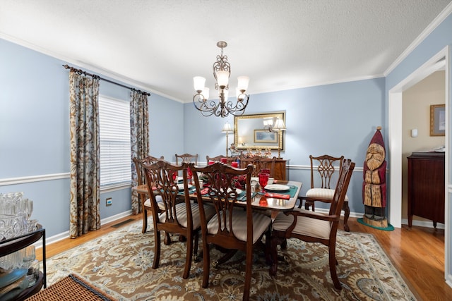 dining area featuring hardwood / wood-style flooring, a notable chandelier, crown molding, and a textured ceiling