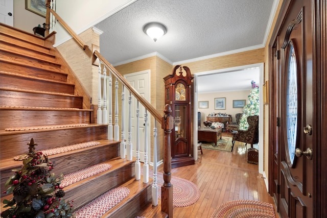 entrance foyer featuring a textured ceiling, light wood-type flooring, and crown molding