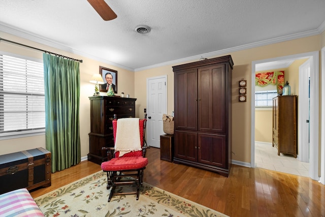 sitting room featuring a textured ceiling, light wood-type flooring, ceiling fan, and ornamental molding