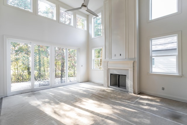 unfurnished living room featuring carpet flooring, a towering ceiling, and ceiling fan