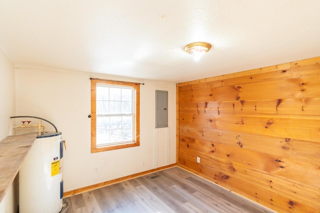 interior space with wooden walls, light hardwood / wood-style floors, electric panel, and water heater